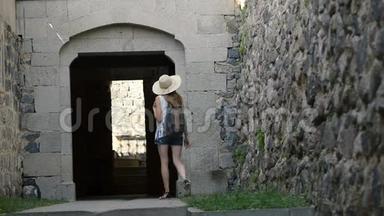 戴着背包的帽子的年轻女子进入了一座古老建筑的拱门。 背面